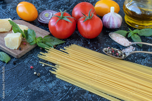 top view on uncooked pasta and products on black background. dry spaghetti with vegetables, herbs and cheese on a wooden table. Soft focus