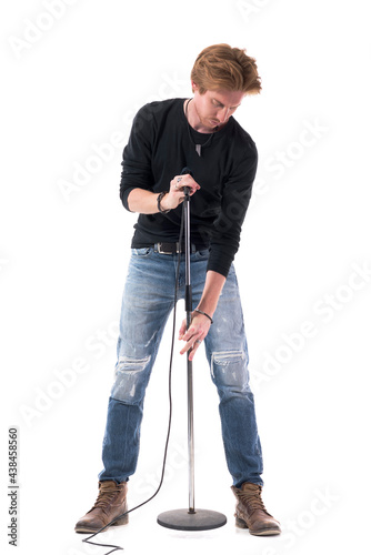 Young good-looking rock singer adjusting microphone stand height. Full body length isolated on white background.