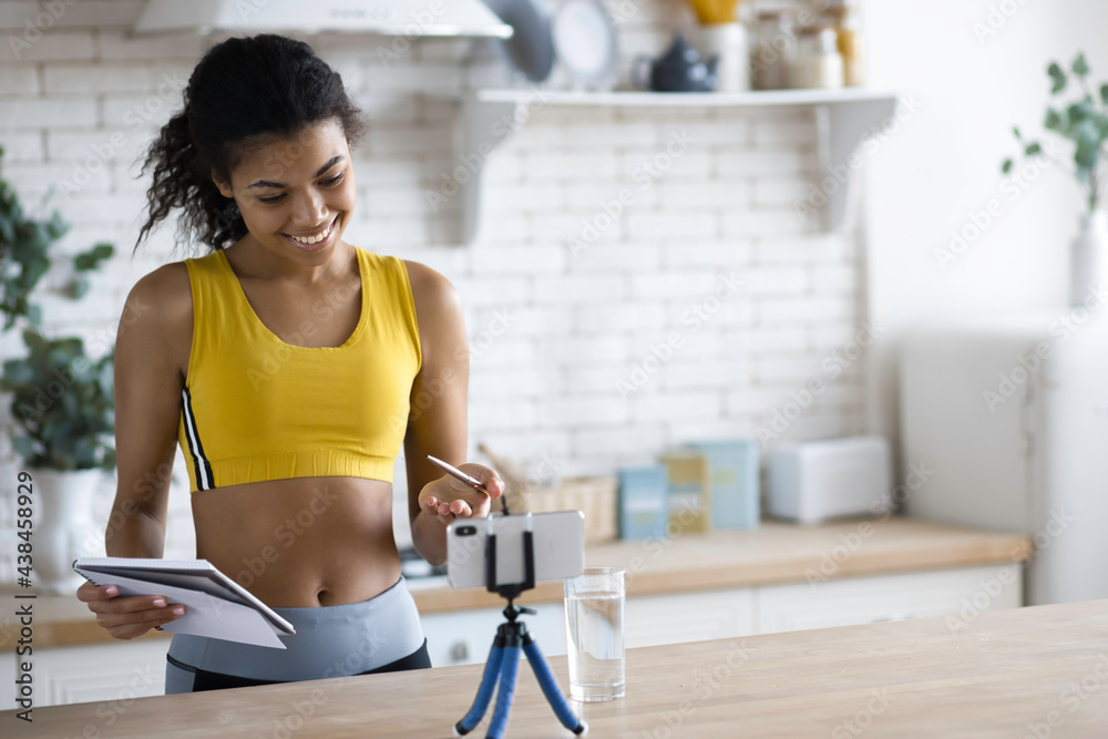 Handsome African American woman fitness vlogger record streaming video about fitness and a healthy lifestyle at home in the kitchen, young female blogger shoot social media vlog on smartphone Handsome African American woman fitness vlogger record streaming video about fitness and a healthy lifestyle at home in the kitchen, young female blogger shoot social media vlog on smartphone