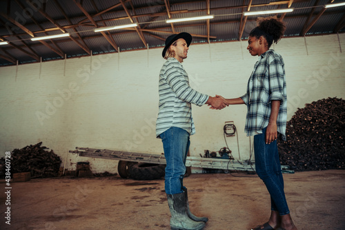 mixed race couple standing in farm shed shaking hands in congratulations after long day of work