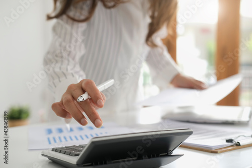 asian businesswoman or accountant working pointing graph discussion and analysis data charts and graphs and using a calculator to calculate  numbers.Business finances and accounting concept photo