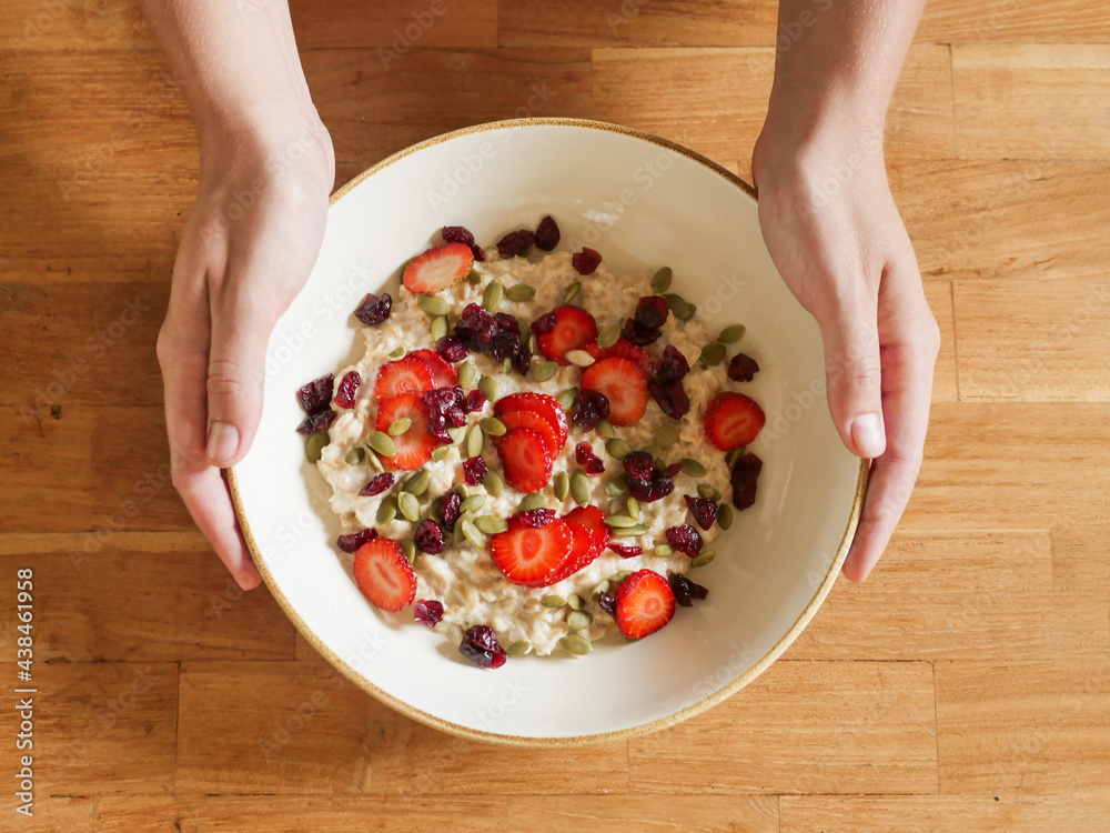 Φωτογραφία Woman's hands hold a bowl of oatmeal with strawberries on a wooden table