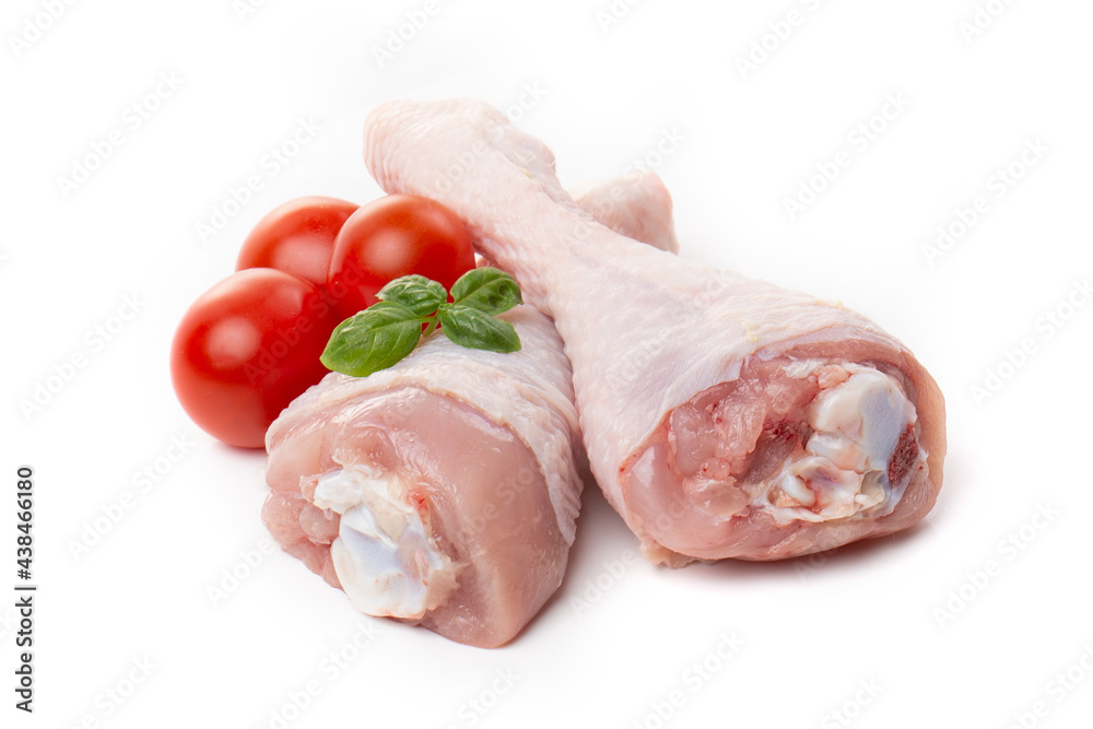 Raw chicken legs with skin decorated with tomatoes and basil on a white background.