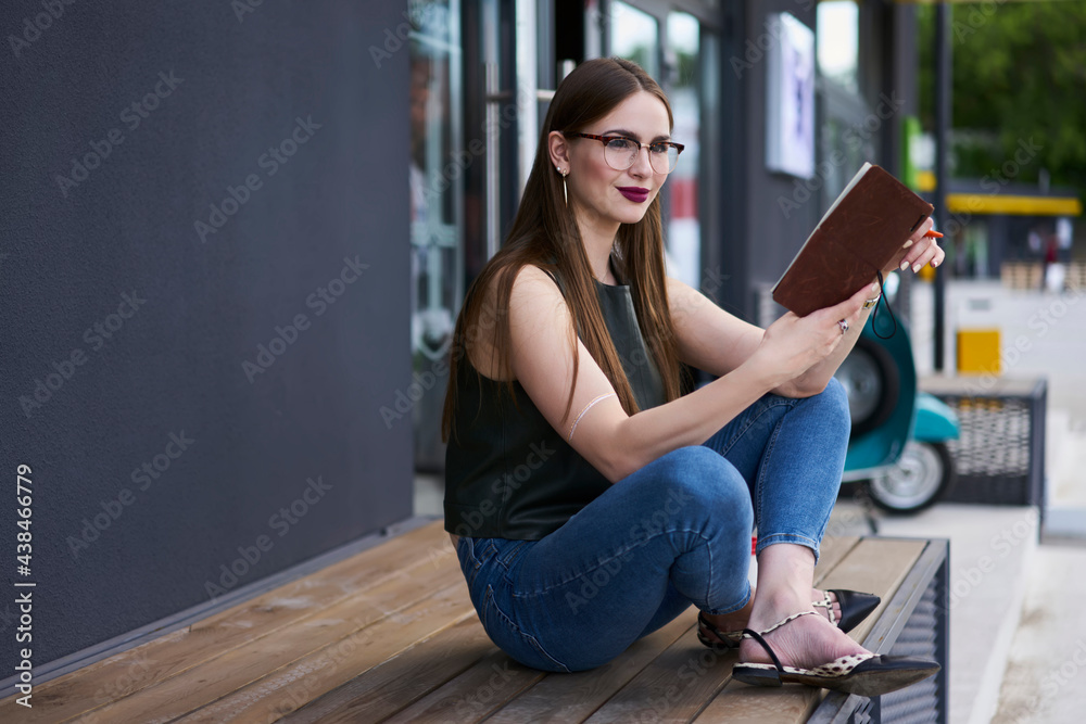 Pondering hipster girl in optical glasses for provide eyes correction thoughtful looking away while thinking about homework task, Caucasian female student with education textbook learning in city Pondering hipster girl in optical glasses for provide eyes correction thoughtful looking away while thinking about homework task, Caucasian female student with education textbook learning in city