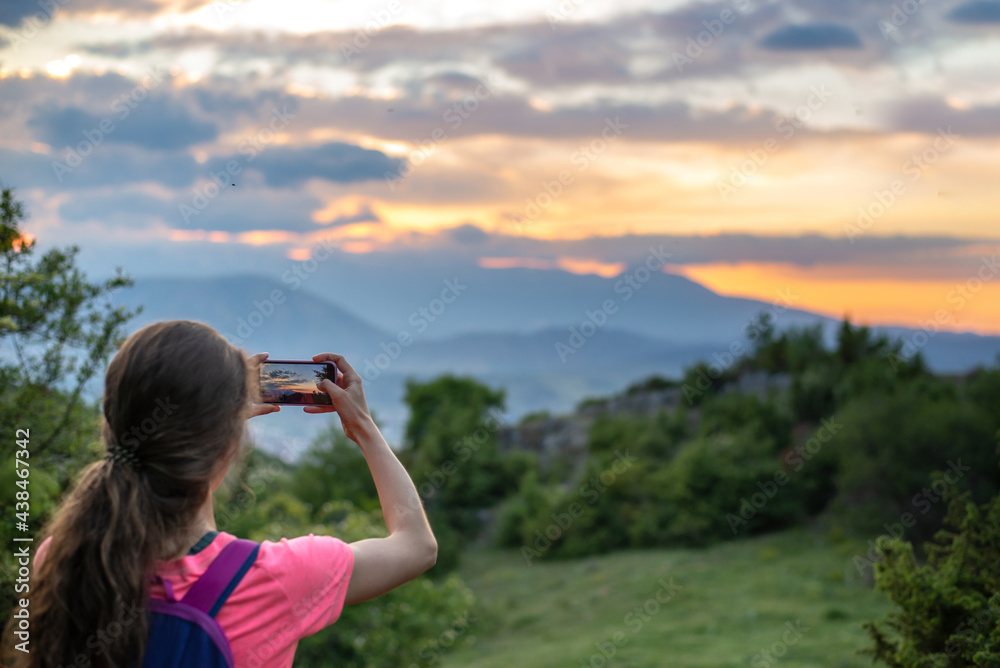 Girl taking photo of a beautiful sunset landscape with her phone, focus on the picture on the screen Girl taking photo of a beautiful sunset landscape with her phone, focus on the picture on the screen