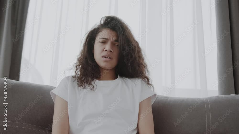 African-American girl got sick, caught a cold, has a flu. The girl sits at home on the couch and sneezes, she wipes her nose with a handkerchief. African-American girl got sick, caught a cold, has a flu. The girl sits at home on the couch and sneezes, she wipes her nose with a handkerchief.