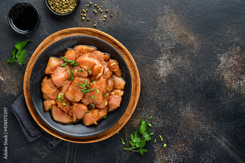 Fotografia Raw chicken meat marinated in teriyaki soy sauce, onions and pepper in a black plate on a dark slate, stone or concrete background