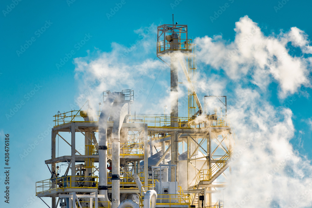 Manufacturing facility with smoke against a blue sky.