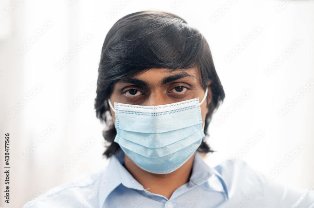 Close-up portrait of serious young indian man wearing surgical medical mask and smart casual blue shirt, eastern man protects himself from virus diseases, preventing spread of corona virus Close-up portrait of serious young indian man wearing surgical medical mask and smart casual blue shirt, eastern man protects himself from virus diseases, preventing spread of corona virus