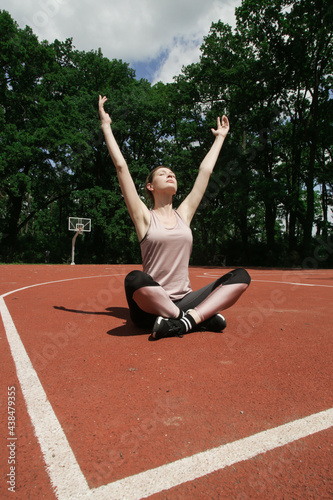 Sportswoman practicing yoga outdoor sitting in Easy Seat pose. Woman sitting cross-legged on the ground with arms raised.