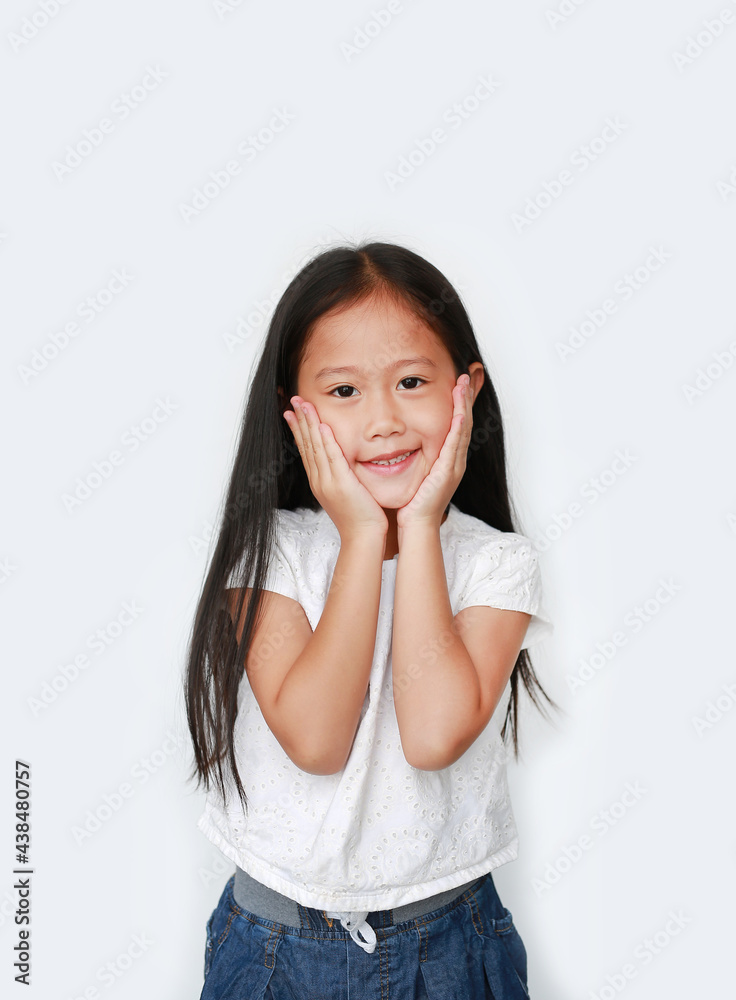 Happy little asian child girl keeps both hands on cheeks over white background with looking at camera. Charming and positive looking. Expresses pleasant emotions. Happy little asian child girl keeps both hands on cheeks over white background with looking at camera. Charming and positive looking. Expresses pleasant emotions.