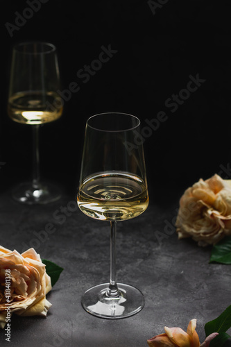 Glass of white wine chardonnay and roses on dark background