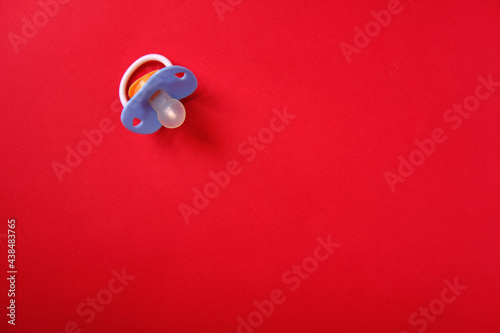 Baby pacifier on a red background, top view, place for an inscription