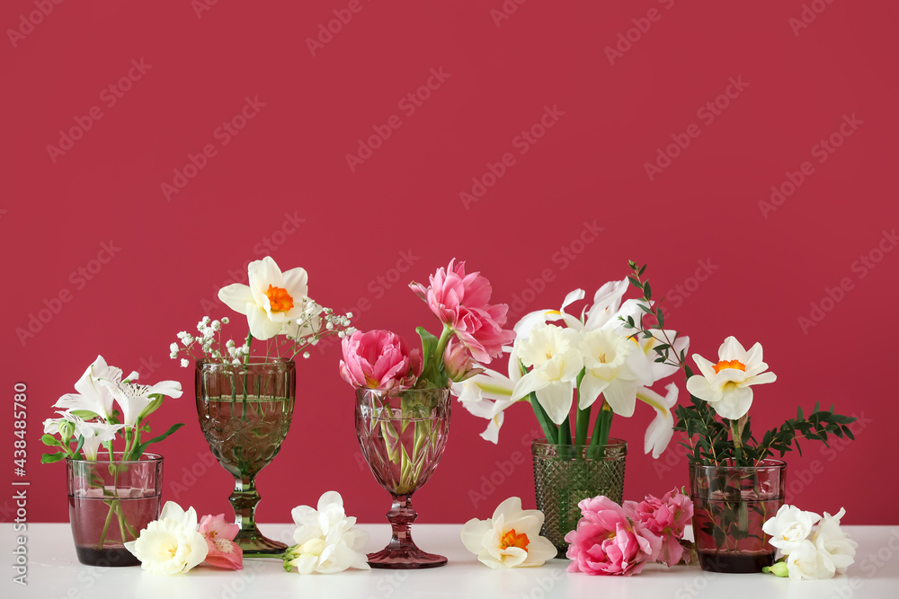 Glasses with beautiful flowers on color background