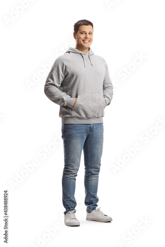 Full length portrait of a young man in a gray hoodie and jeans posing with hands in pockets
