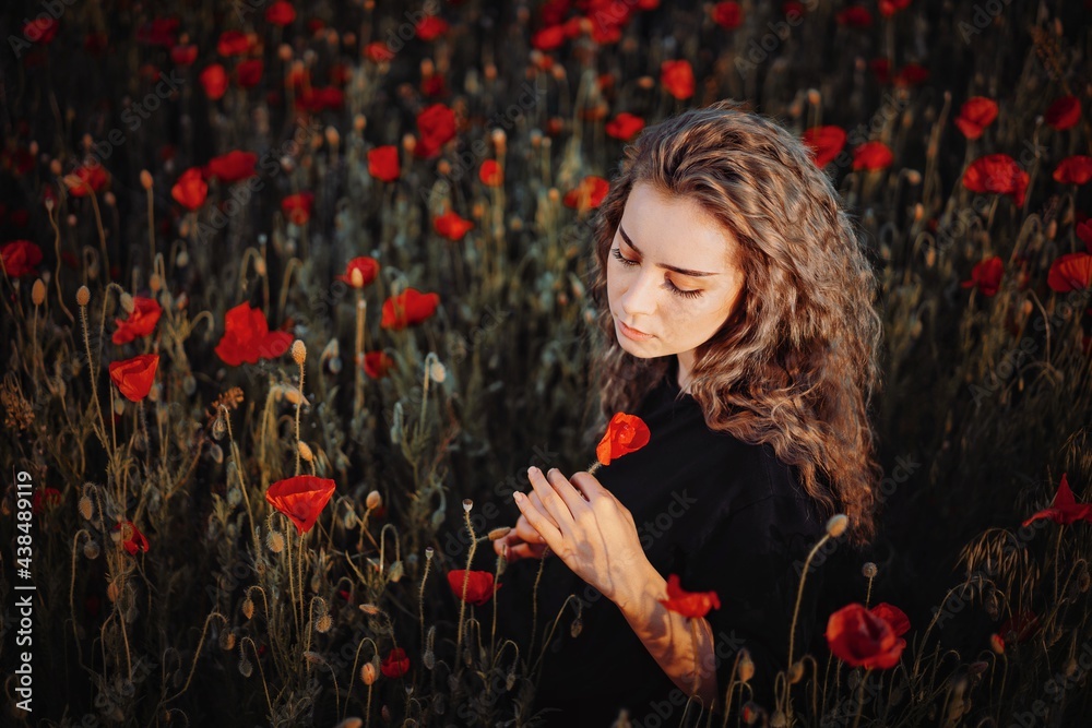 Naklejka premium Beautiful young woman with poppy in field
