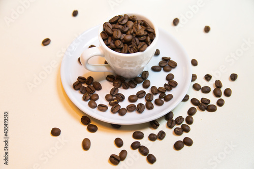 White cup on saucer filled with brown coffee beans on a white background. Confectionery products drinks tea coffee.