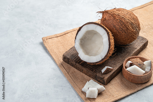 A whole and open coconut with pieces on a gray background.