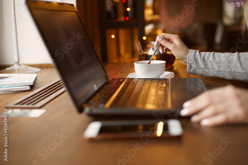 Girl ordering tea in a cafe. Works for a laptop. The mobile phone is on the table. Remote work and freelance work concept.