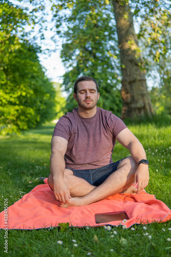 Obraz na płótnie Photo of a young and attractive man sitting on a towel with his eyes closed and his legs crossed meditating in the middle of nature. Enjoying silence, relaxing with a guided meditation w salonie