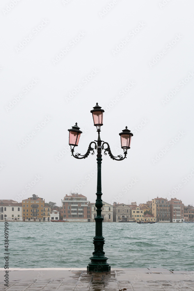 Alte Straßenlaterne auf Giudecca in Venedig mit der  Silhouette von Venedig im Hintergrund bei Hochwasser