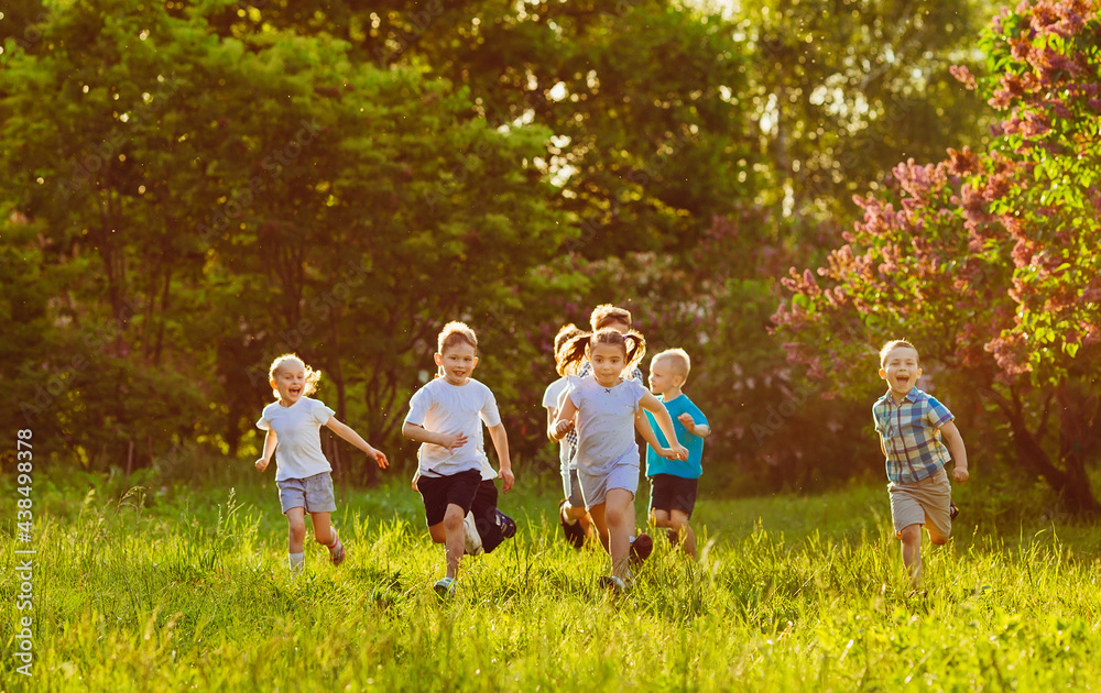Fototapeta premium A group of happy children of boys and girls run in the Park on the grass on a Sunny summer day.