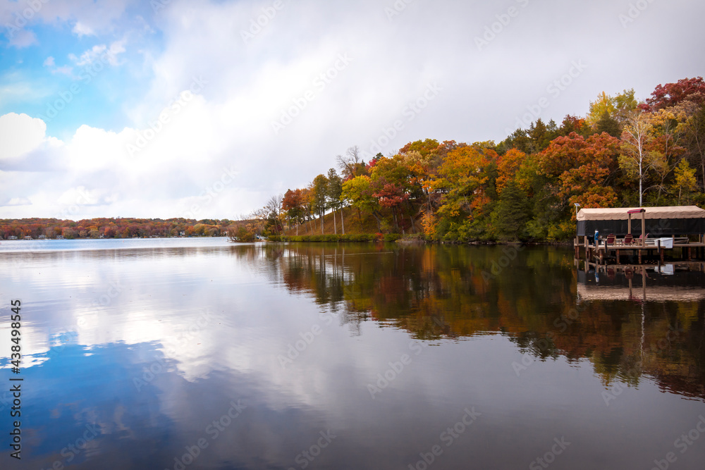 The wind is calm on a Wisconsin lake in fall.  The colors of the trees and the partly cloudy sky is reflected in the lake's surface.