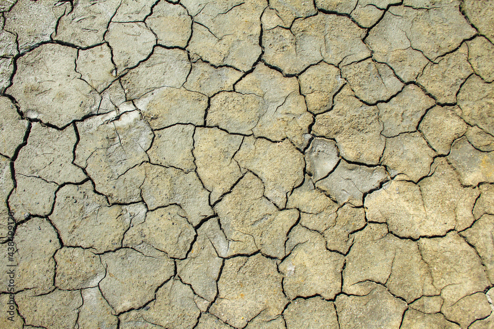 Dried brown clay surface covered with cracks. A bright, sunny day. Harsh shadows. Top view, textured, background.