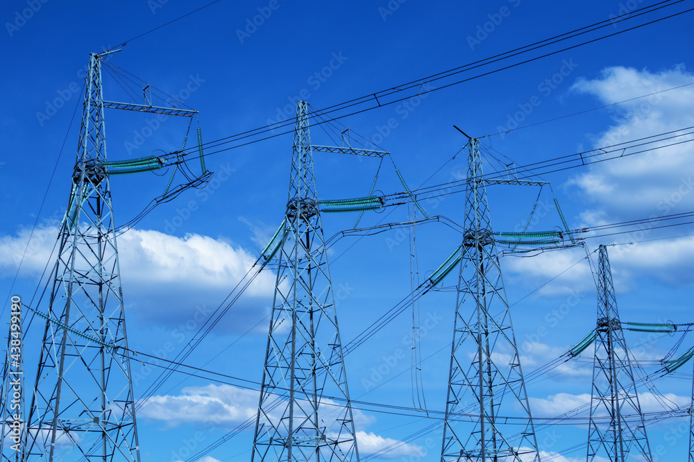 A group of high voltage power transmission towers against a background of blue sky and clouds. Wires with insulators are connected to metal structures. Part of a large network. Sale of electricity