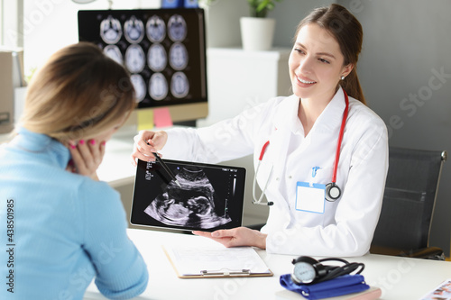 Woman obstetrician gynecologist showing patient photograph of ultrasound examination of fetus on digital tablet photo