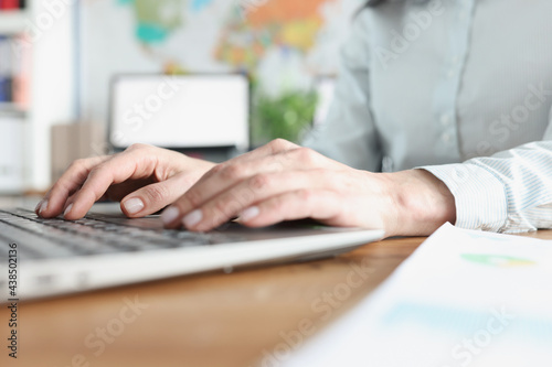 Female hands typing on laptop keyboard in office closeup
