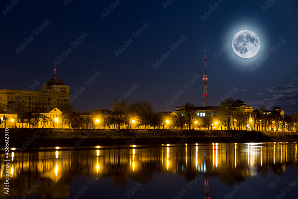 Full moon over the city. Night landscape. Lantern lights are reflected in water. Supermoon.