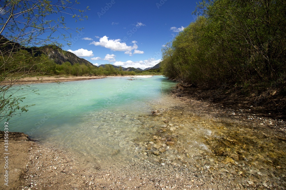 clear water creekflows into turquoise water river with green bushes and wooded hills around, blue sky and few white clouds