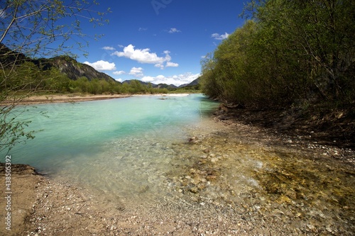 clear water creekflows into turquoise water river with green bushes and wooded hills around  blue sky and few white clouds