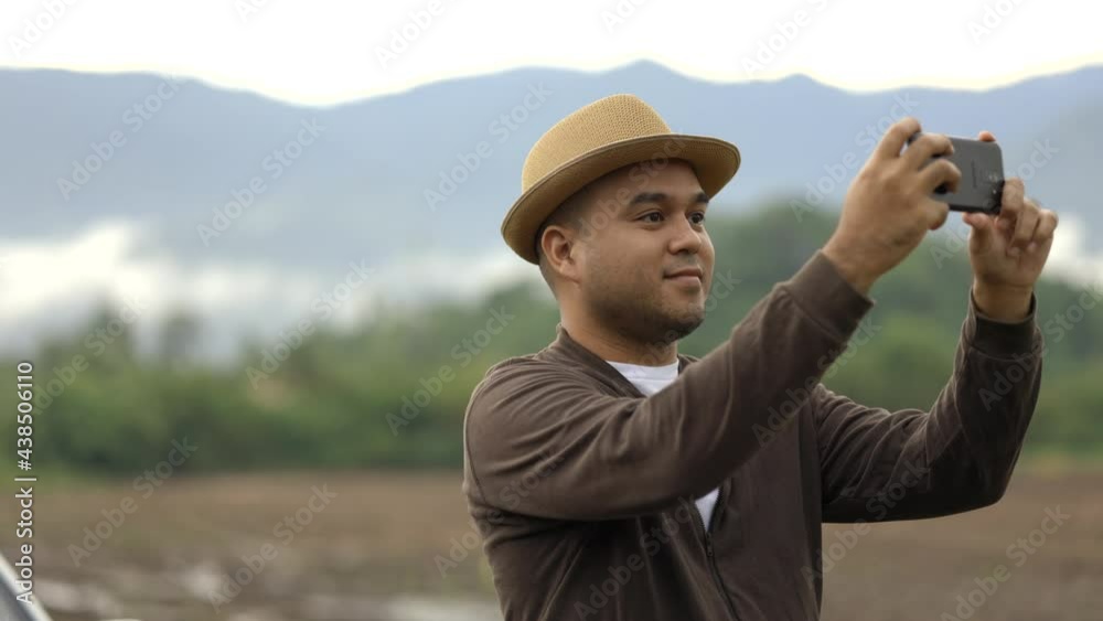 Young Asian men travel to beautiful nature. He was standing on the roadside. He uses his phone to take pictures of beautiful views. Young Asian men travel to beautiful nature. He was standing on the roadside. He uses his phone to take pictures of beautiful views.
