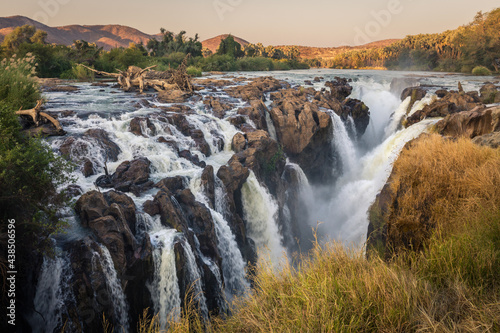 Epupa falls, Namibian side, Angola border.  Multiple rivulets and cascading waters in soft evening light, ramed by grassy foreground. Water flow frozen with a moderate shutter speed.