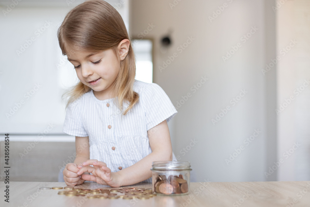 Little girl putting coins into glass jar indoors. Money savings concept. Little girl putting coins into glass jar indoors. Money savings concept.