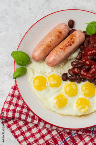 Top view of served English breakfast of fried eggs and sausages with red beans and tomato sauce