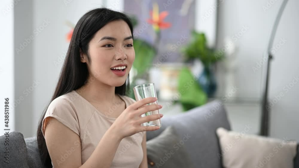 Healthy pretty asian brunette girl, holding and drinking a glass of pure water, while sitting at home on sofa in casual t-shirt, leading a healthy lifestyle, smiling Healthy pretty asian brunette girl, holding and drinking a glass of pure water, while sitting at home on sofa in casual t-shirt, leading a healthy lifestyle, smiling