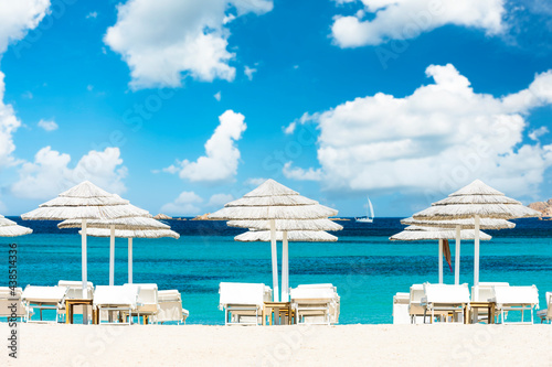 Fototapeta Naklejka Na Ścianę i Meble -  (Selective focus) Stunning view of some white thatch umbrellas and sunbeds on a white sand beach bathed by a beautiful, turquoise sea. Romazzino Beach, Porto Cervo, Sardinia, Italy.