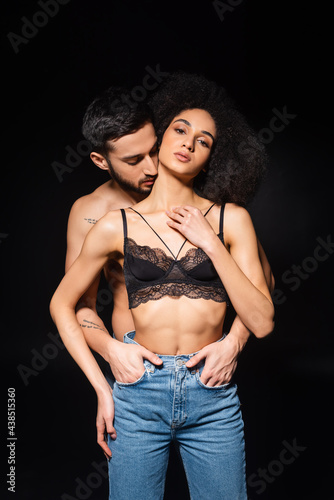 Bearded man kissing neck of african american woman in jeans and bra isolated on black