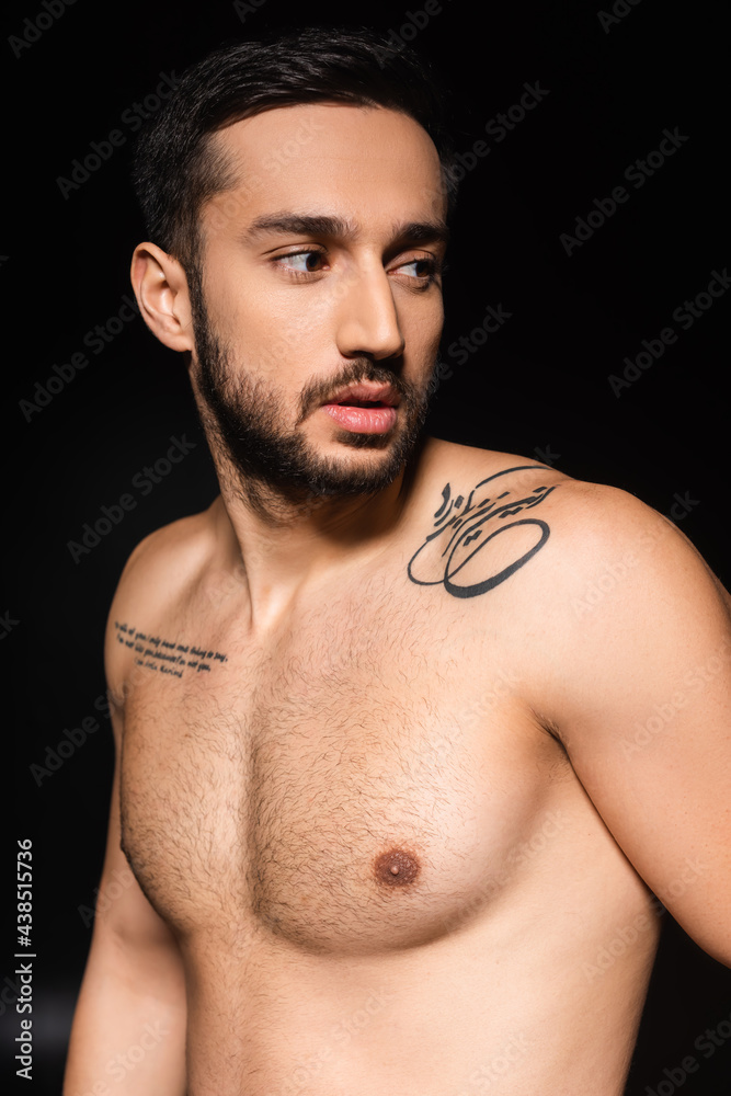 Tattooed man with shirtless torso looking away isolated on black Tattooed man with shirtless torso looking away isolated on black