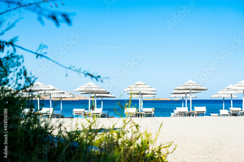 (Selective focus) Stunning view of some white thatch umbrellas and sunbeds on a white sand beach bathed by a beautiful, turquoise sea. Romazzino Beach, Porto Cervo, Sardinia, Italy.