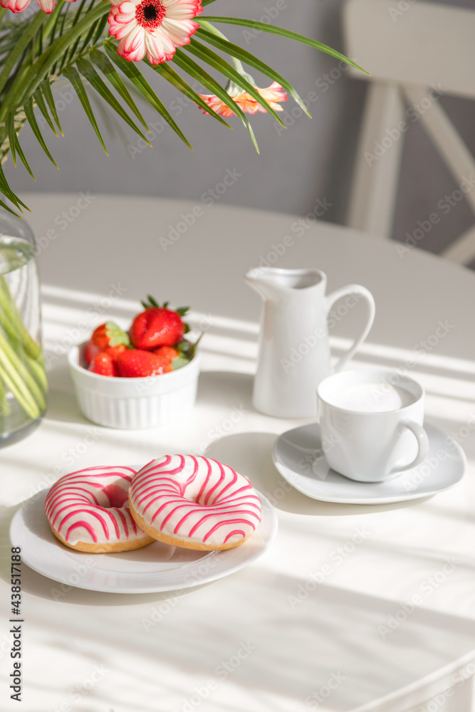 Romantic breakfast in the kitchen with a bouquet of flowers, donuts, coffee and fresh strawberries. Brunch on a sunny day