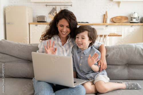 Happy mom and son communicate using video connection with grandparents or dad on business trip. Mom or older sister and little kid call online, cheerful wave hands to computer during conference call