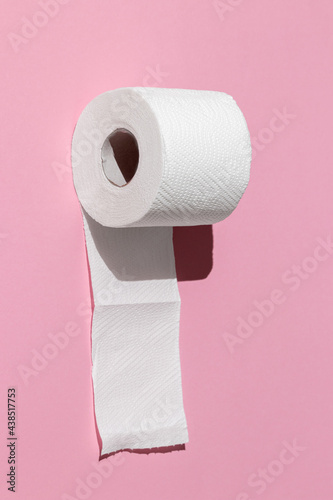 roll of a white toilet paper isolated on a pink background close-up. hard shadows from the sun at noon