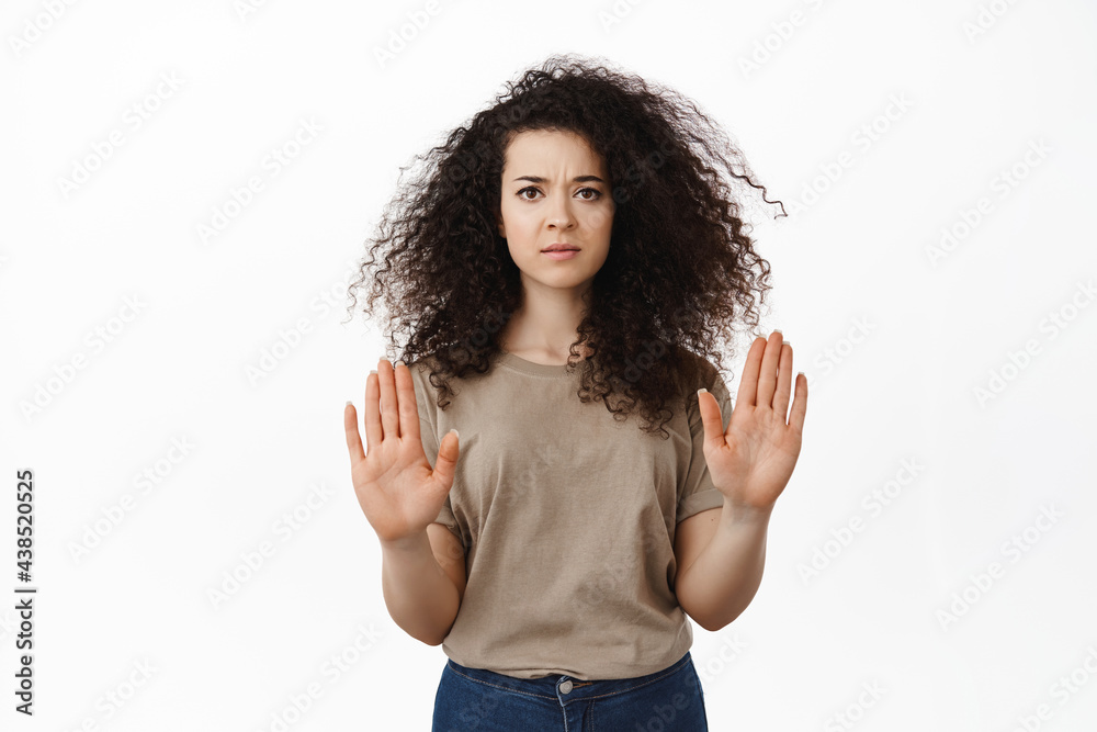 Stop this. Serious concerned woman showing no, block gesture, raising hands to disapprove and decline bad offer, rejecting you, standing against white background Stop this. Serious concerned woman showing no, block gesture, raising hands to disapprove and decline bad offer, rejecting you, standing against white background