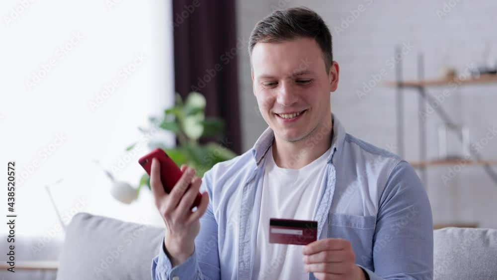 Handsome young Caucasian male shopping with a credit card at home. Man buying online on his smartphone while paying with a credit card. Internet shopping alone at home, secure safe payments concept. Handsome young Caucasian male shopping with a credit card at home. Man buying online on his smartphone while paying with a credit card. Internet shopping alone at home, secure safe payments concept.