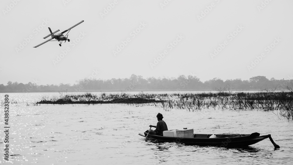 View of the lake with a low flying airplane and fisherman on a boat in the lake