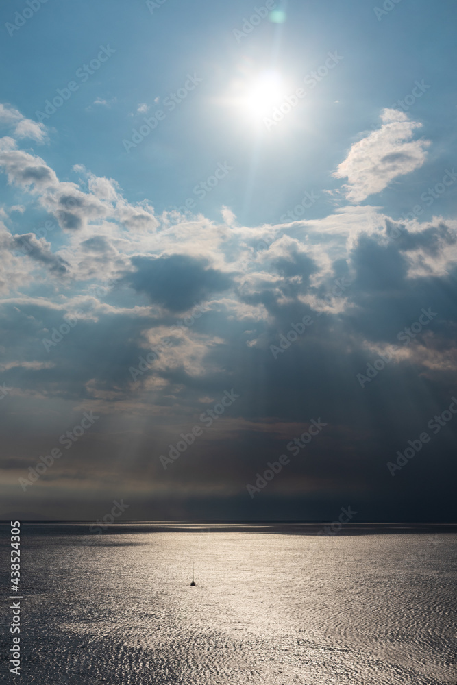 Sun rays shining though clouds over the sea in Greece. Dramatic cloudscape on mediterranean sea water surface. Vertical Sun rays shining though clouds over the sea in Greece. Dramatic cloudscape on mediterranean sea water surface. Vertical